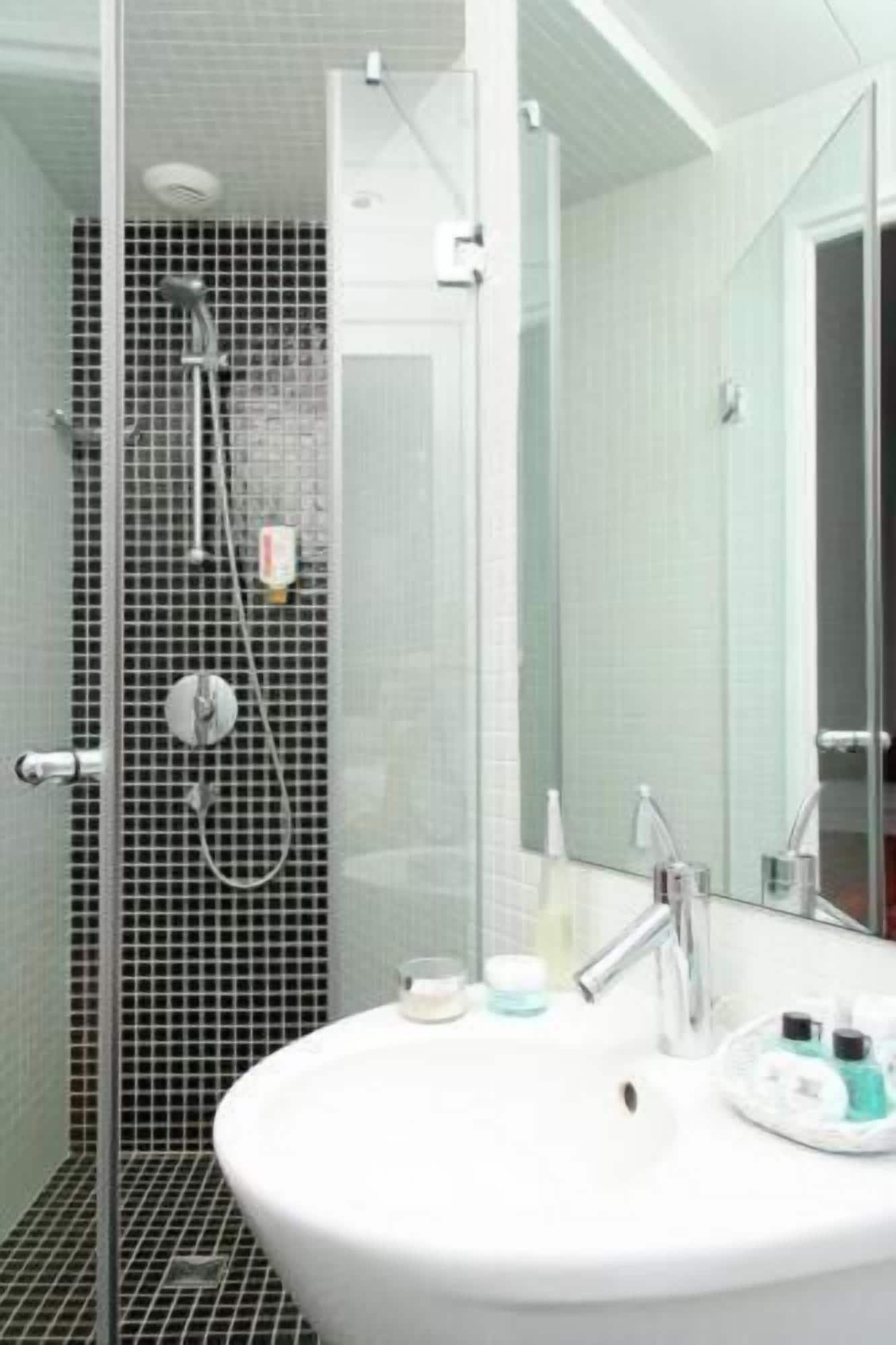 A bathroom with a glass shower enclosure, a white sink with toiletries, and a mirror.