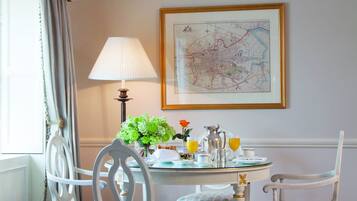 A dining area with a table set for two, a lamp, a vase with flowers, and a framed map on the wall.