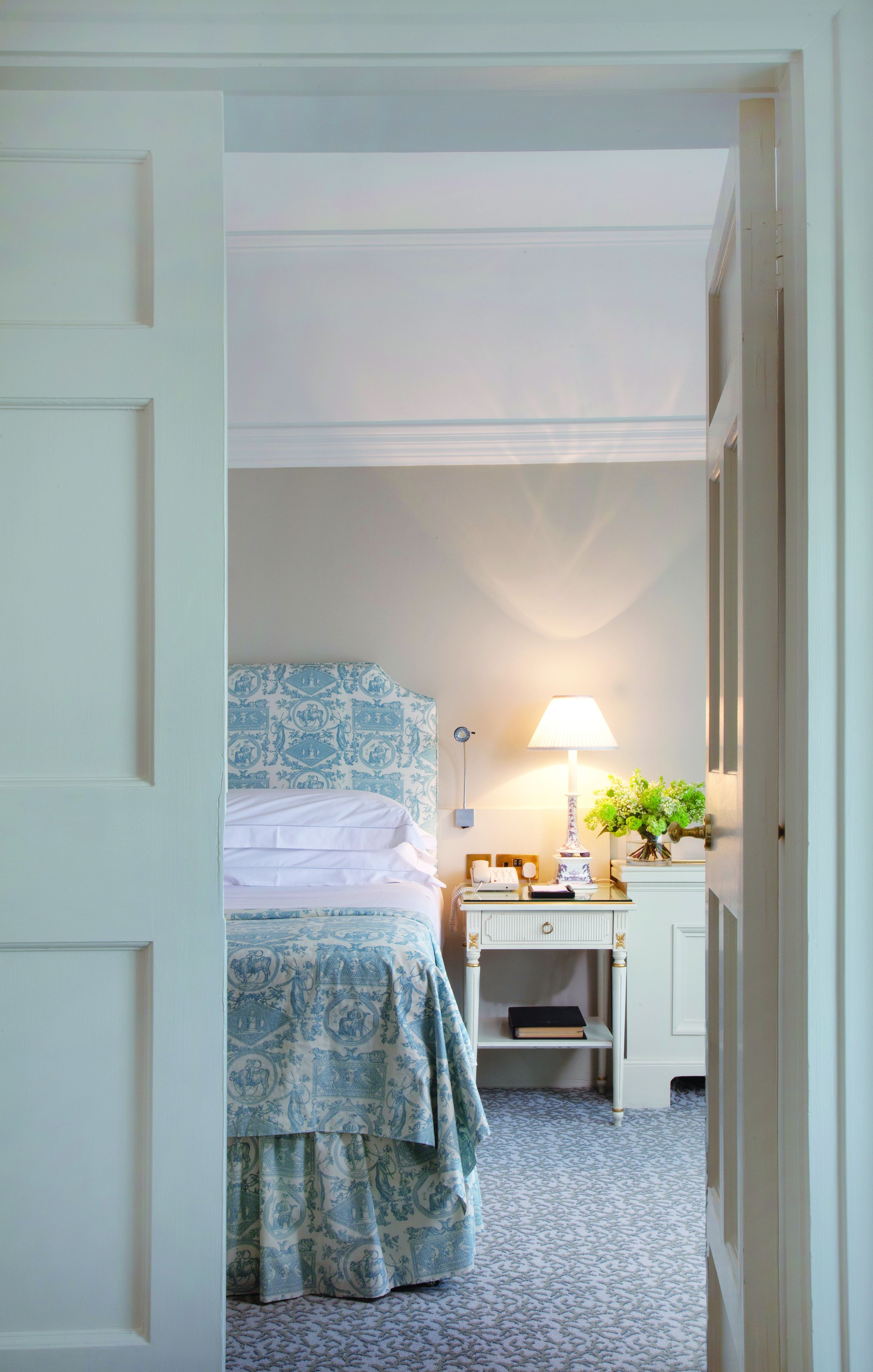 Ein Schlafzimmer mit Bett, Nachttisch, Lampe und einem kleinen Regal mit Büchern.