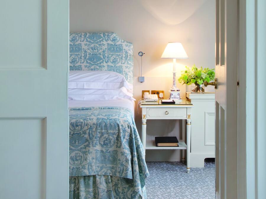 Ein Schlafzimmer mit Bett, Nachttisch, Lampe und einem kleinen Regal mit Büchern.