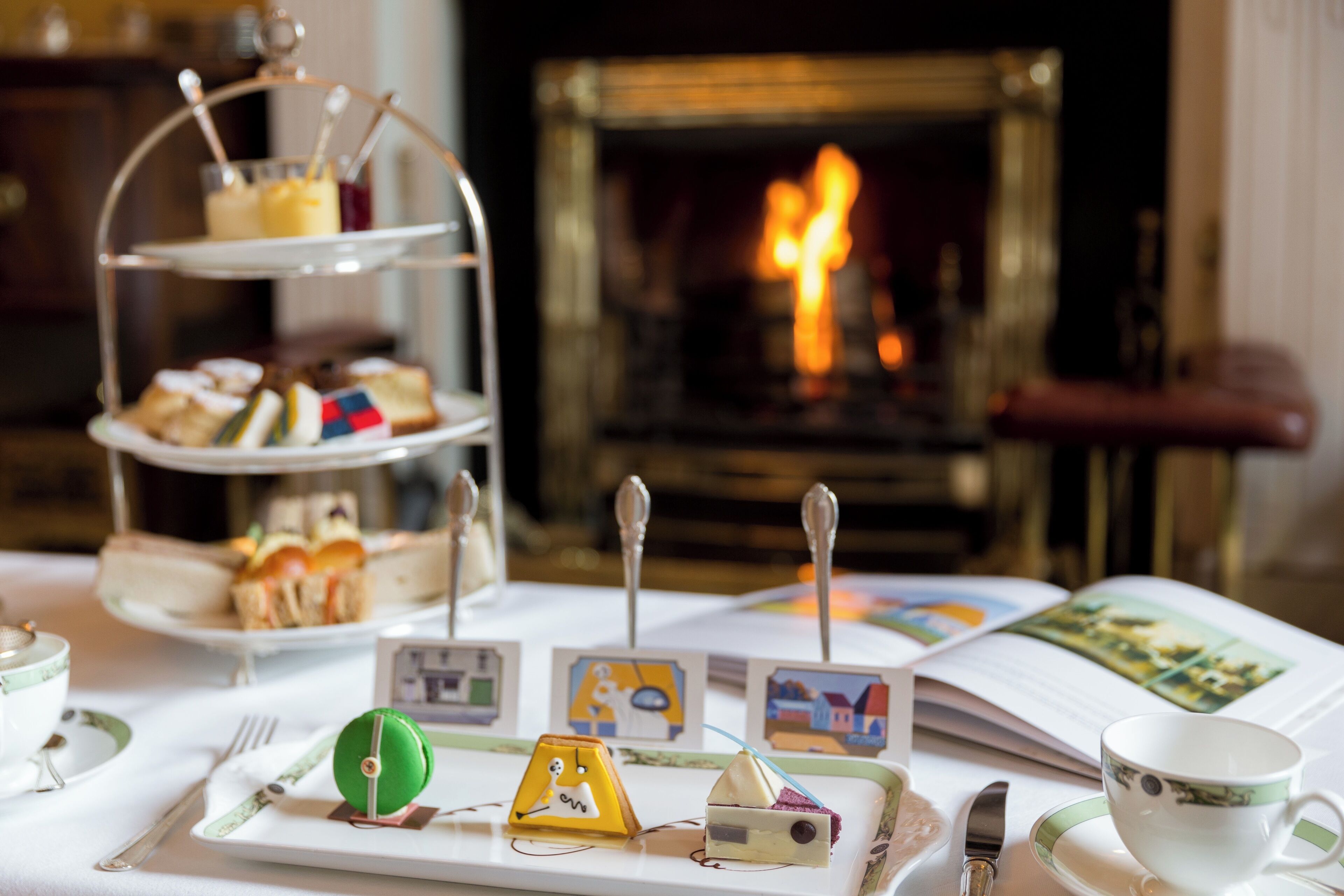 A table with a tiered dessert stand, a book, and a cup.