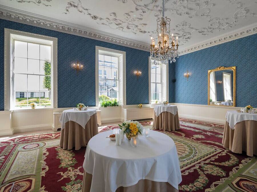A room with large windows, a chandelier, and tables set for a formal event.