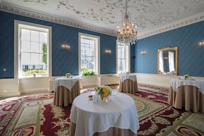 A room with large windows, a chandelier, and tables set for a formal event.