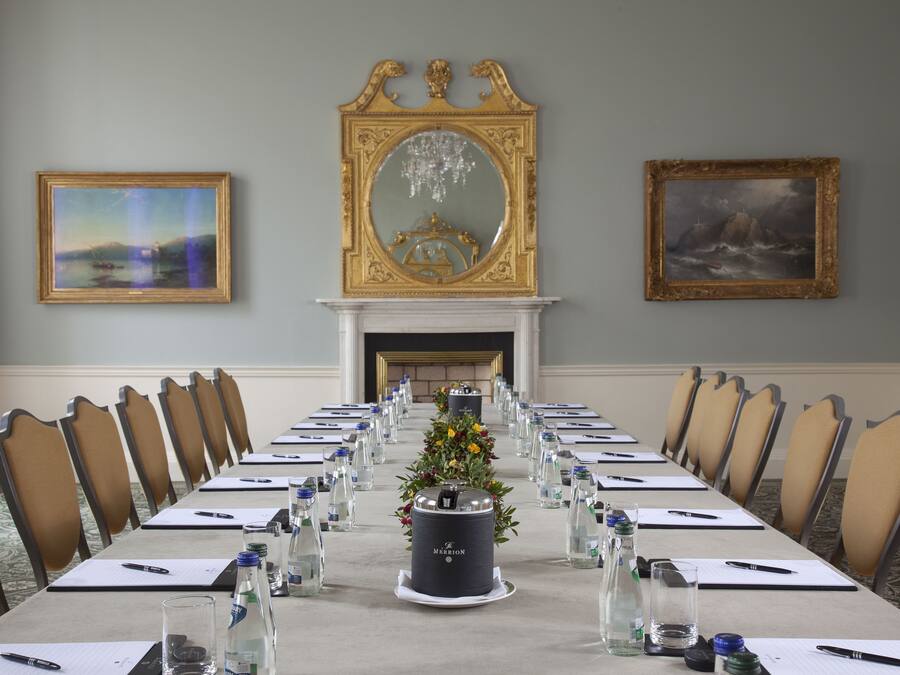 Een vergaderruimte met een lange tafel, stoelen, waterflesjes en een decoratief middelpunt.