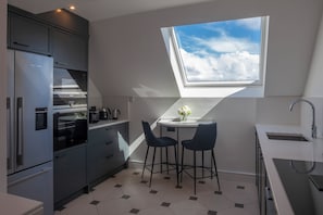 A modern kitchen with a skylight, two bar stools, and a built-in oven.