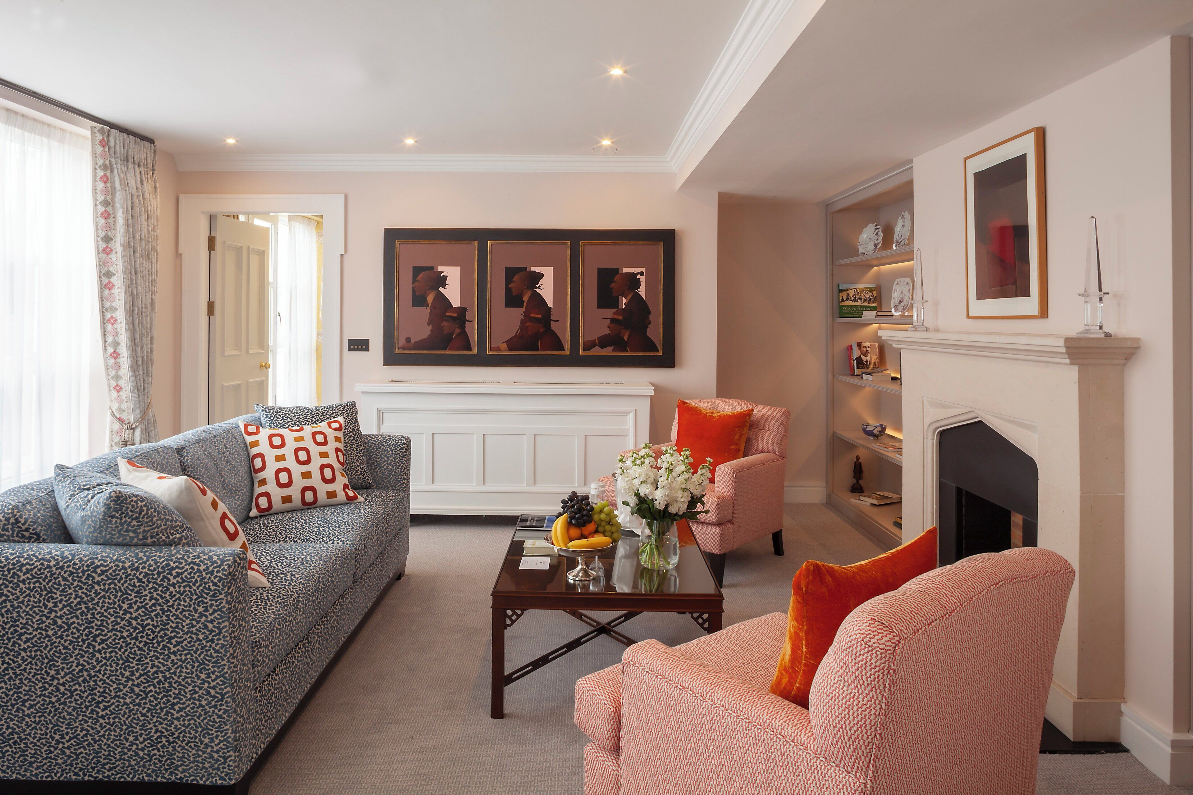 A living room with a sofa, armchair, coffee table, and fireplace. There are framed pictures on the wall and a vase with flowers on the coffee table.