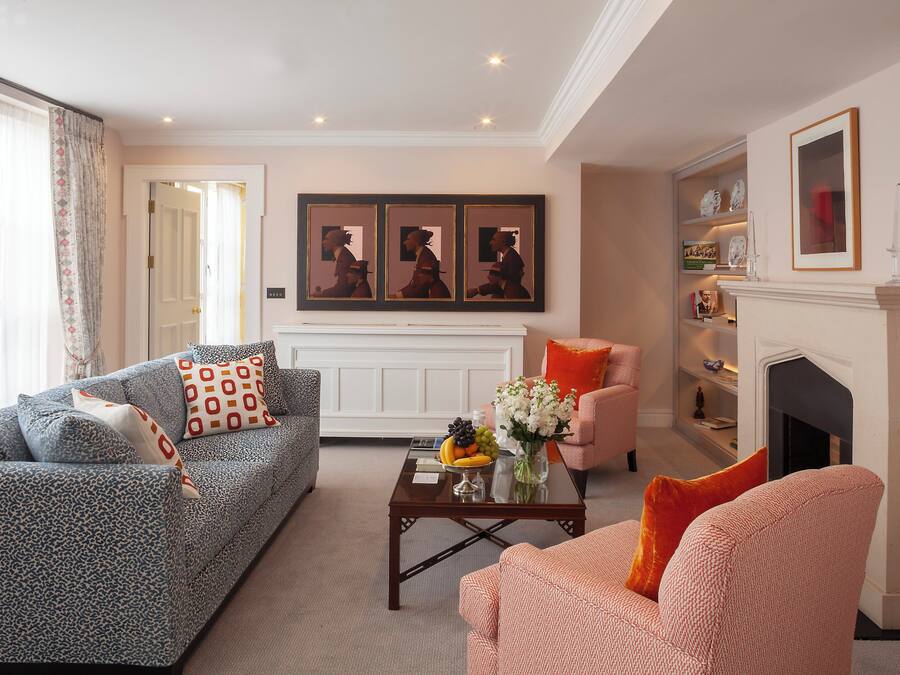 A living room with a sofa, armchair, coffee table, and fireplace. There are framed pictures on the wall and a vase with flowers on the coffee table.