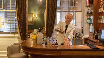 A bar area with a bartender preparing a drink, a large mirror, and a view of the city through the window.