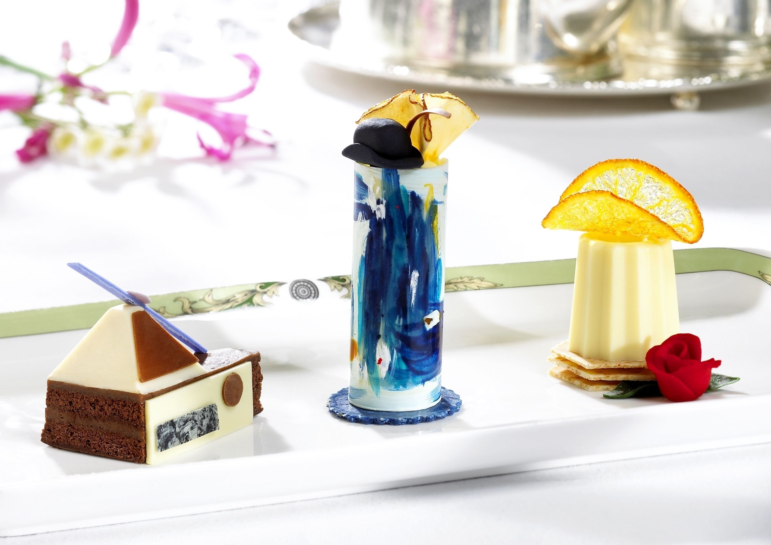 Una mesa de postres con un pastel de chocolate, una bebida azul y blanca, y una bebida amarilla con una rodaja de naranja.