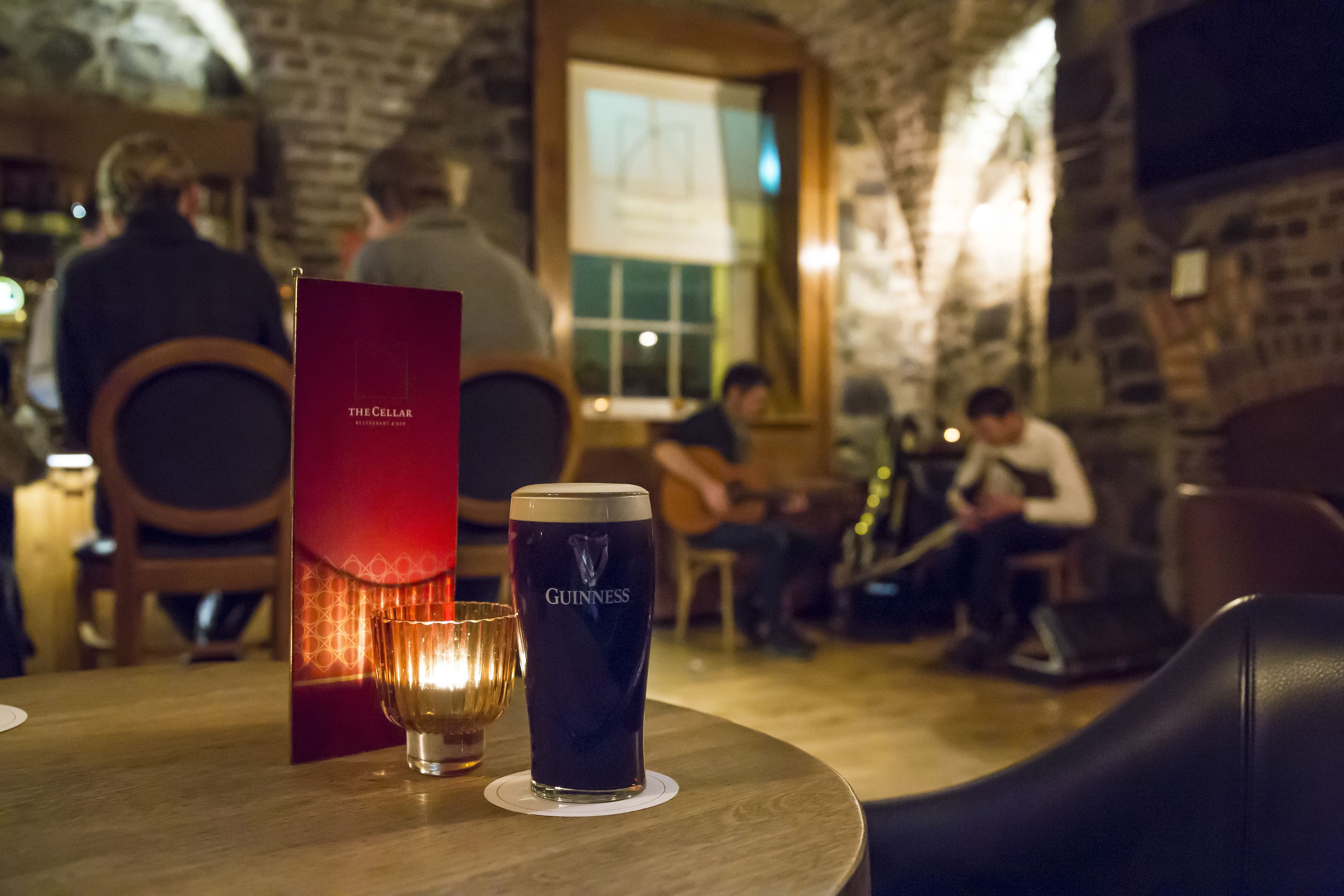 Una mesa de madera con una jarra de cerveza Guinness, un menú y una vela.