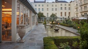 A courtyard with a pool, potted plants, and a building with large windows. - The Merrion (Dublin)