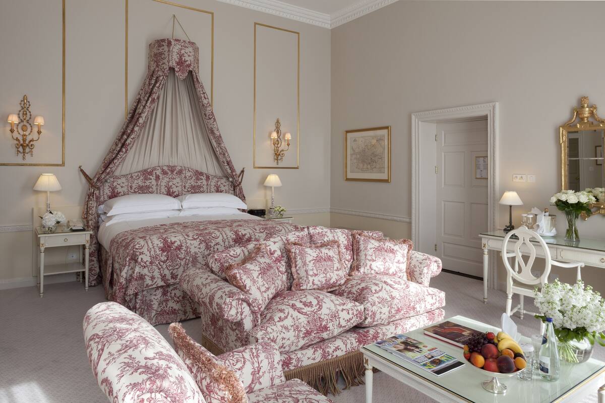 Una camera da letto con un letto a baldacchino, una panca abbinata, un comodino con una lampada, uno specchio e un'arrangiamento floreale su un tavolino.
