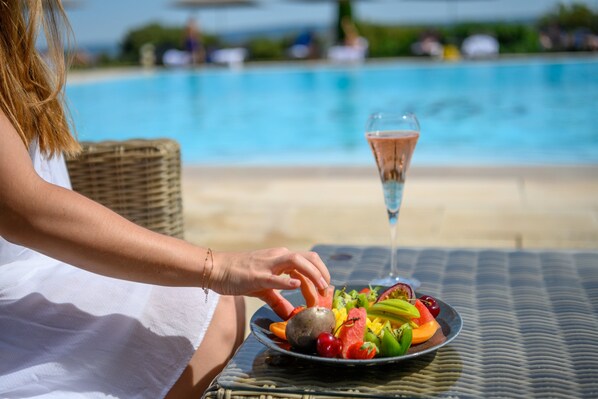 A person sitting by a poolside table with a plate of fruit and a glass of champagne. - Hotel Les Bories & Spa (Gordes)