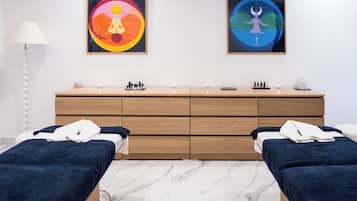 Two single beds with dark linens and white pillows, a dresser, and framed artworks create a calm and inviting space.