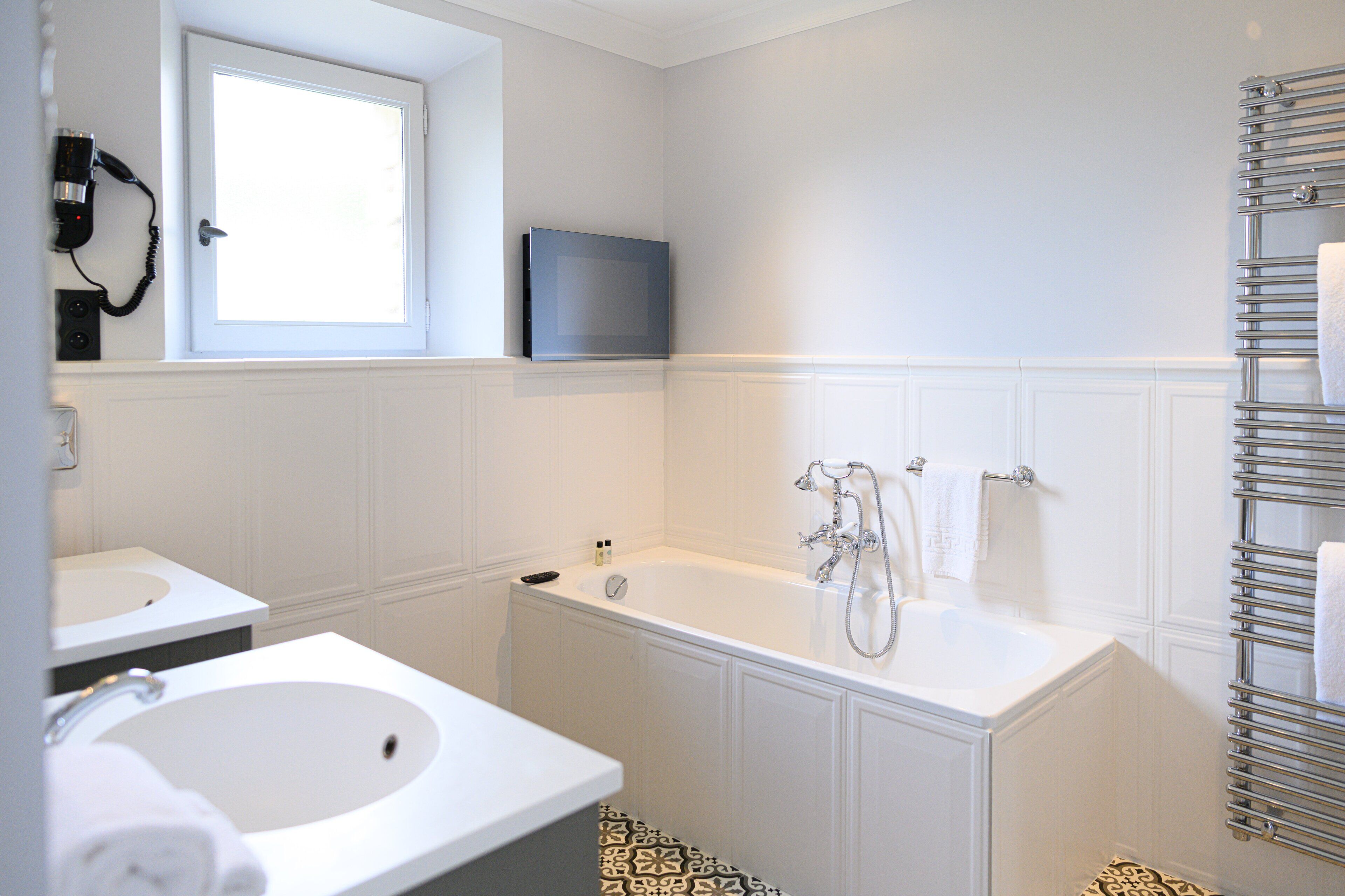 Un baño moderno con un lavamanos blanco, una bañera y una ducha. Hay una ventana sobre el lavamanos y un perchero cerca de la ducha.