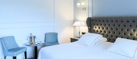 Une chambre d’hôtel avec un grand lit, deux chaises, une petite table avec une lampe et un luminaire fixé au mur.