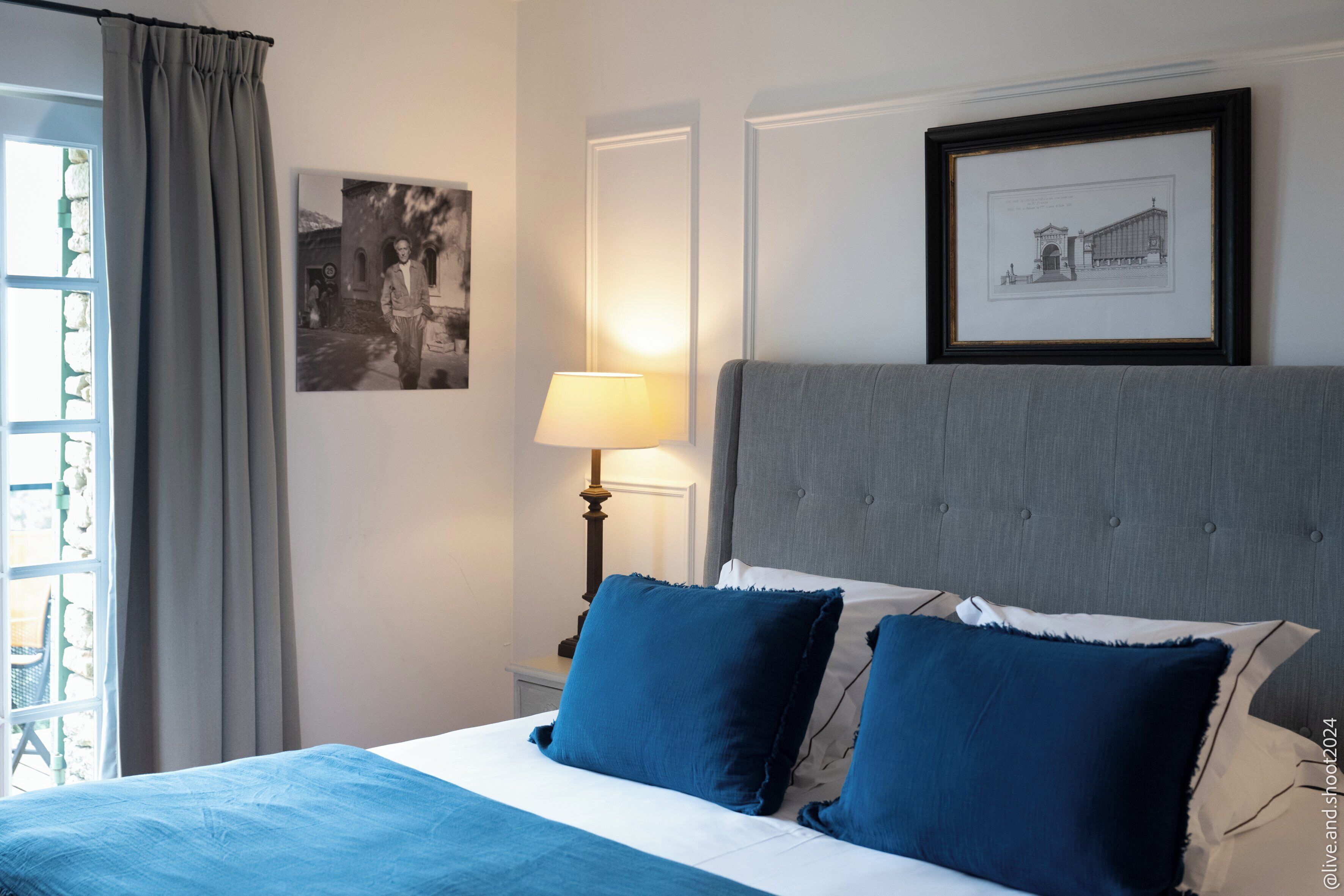 A neatly made bed with blue bedding, a bedside lamp, and a framed picture on the wall.