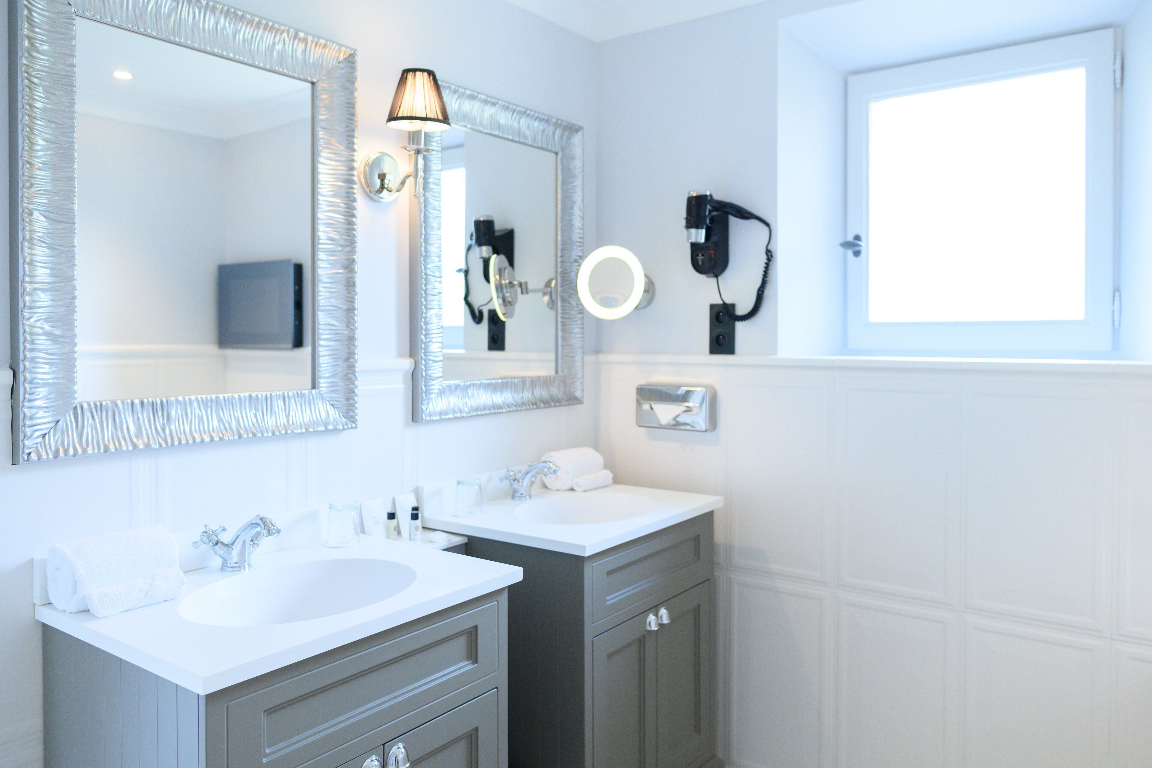A modern bathroom with two sinks, a large mirror, and a hairdryer mounted on the wall.
