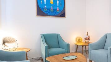 A modern living room with teal armchairs, a wooden coffee table, and a wall-mounted painting.