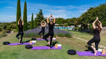 Tres personas practicando yoga al aire libre sobre esterillas moradas, con árboles y un cielo despejado de fondo.