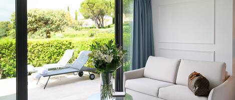 Una sala de estar moderna con un sofá blanco, una mesa de vidrio con un florero y vistas a un jardín a través de grandes ventanales.