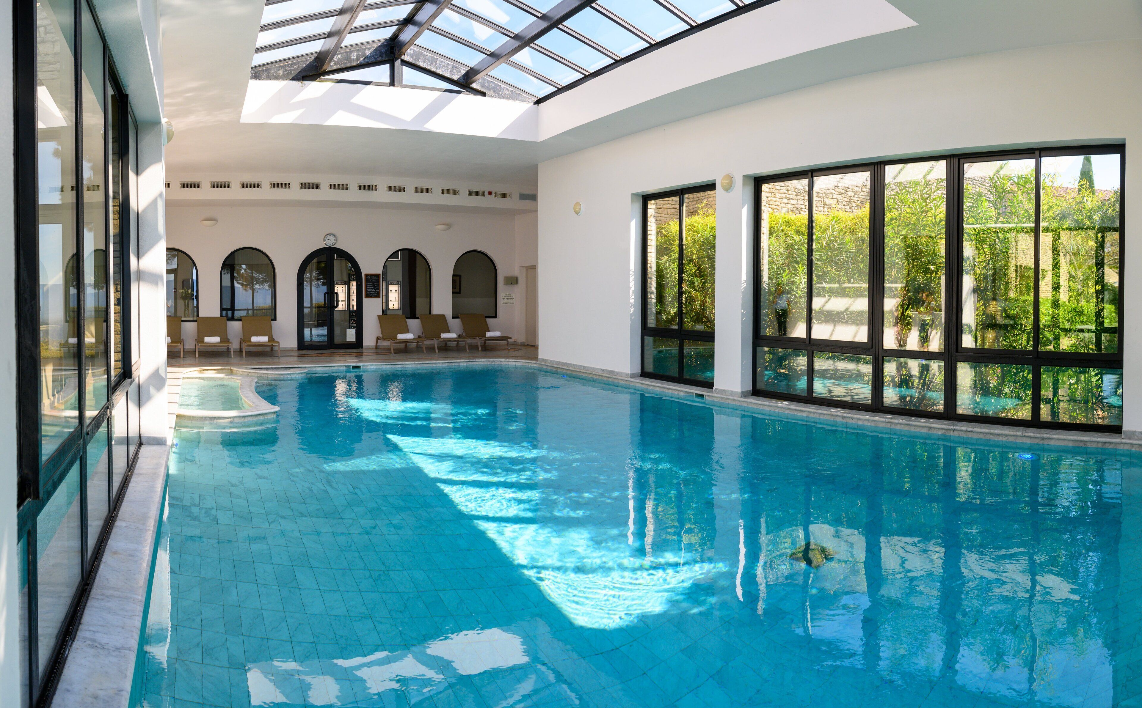 An indoor swimming pool with clear blue water, large windows, and a skylight.