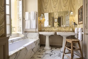 A luxurious bathroom with a marble bathtub, two sinks, and a large mirror.