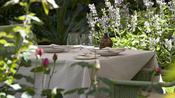 Una mesa al aire libre con mantel blanco, rodeada de follaje y flores.