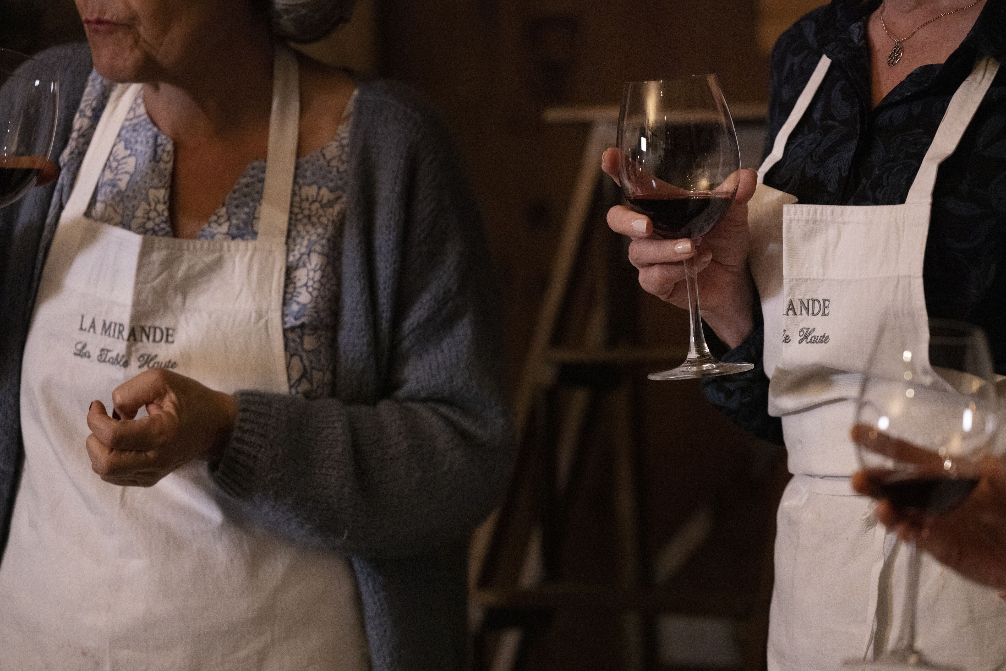 Two people holding wine glasses, wearing aprons with text on them.