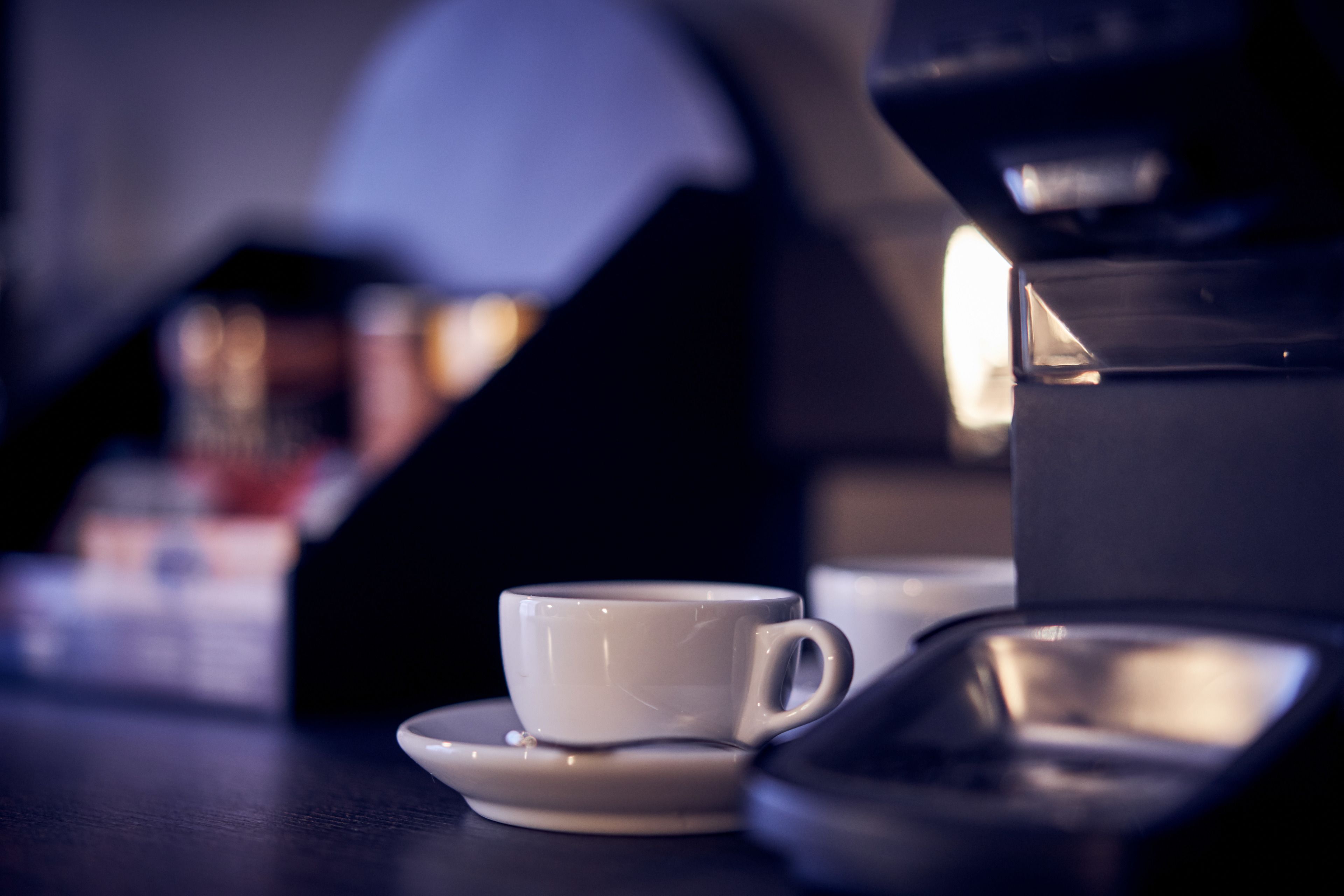 A cup and saucer on a table with a coffee maker in the background.