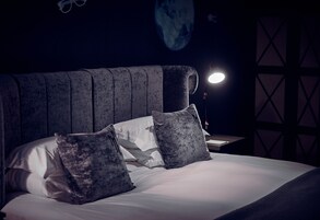 Una cama bien hecha con cabecera, dos almohadas y una mesita de noche con lámpara.