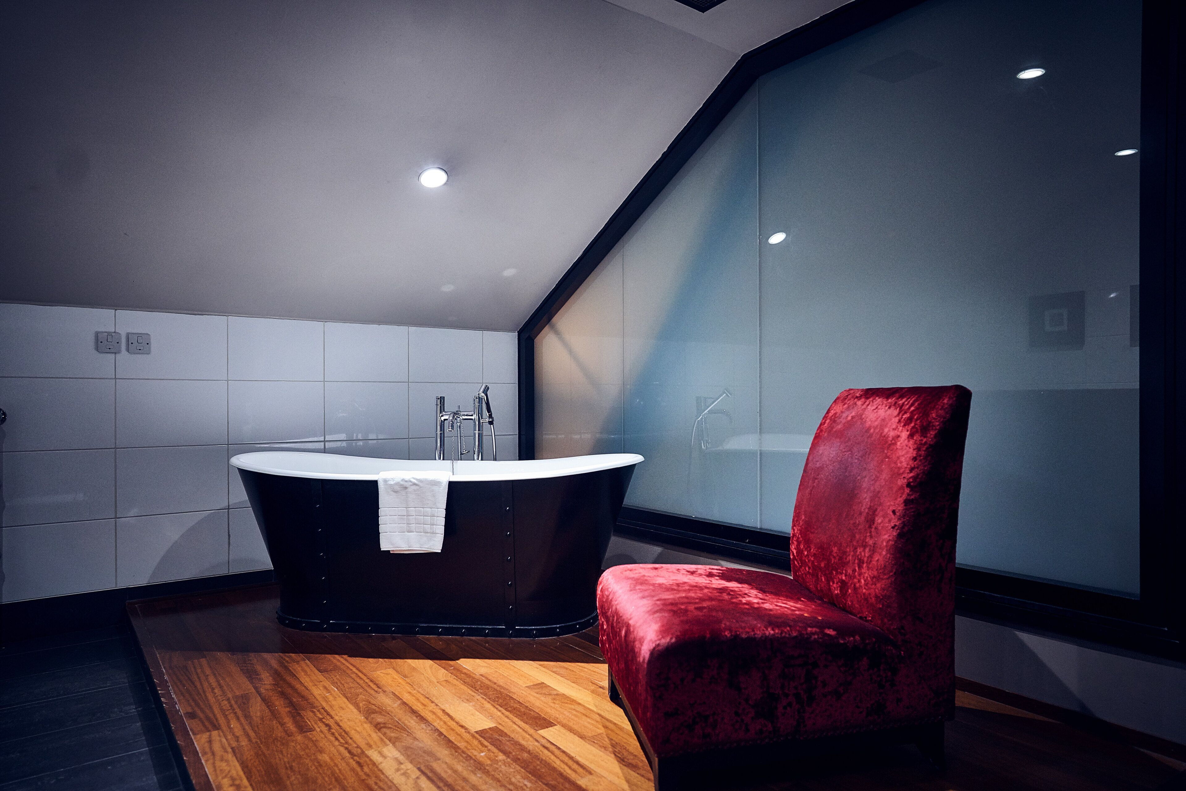 A modern bathroom with a freestanding bathtub, a red upholstered chair, and a large window.