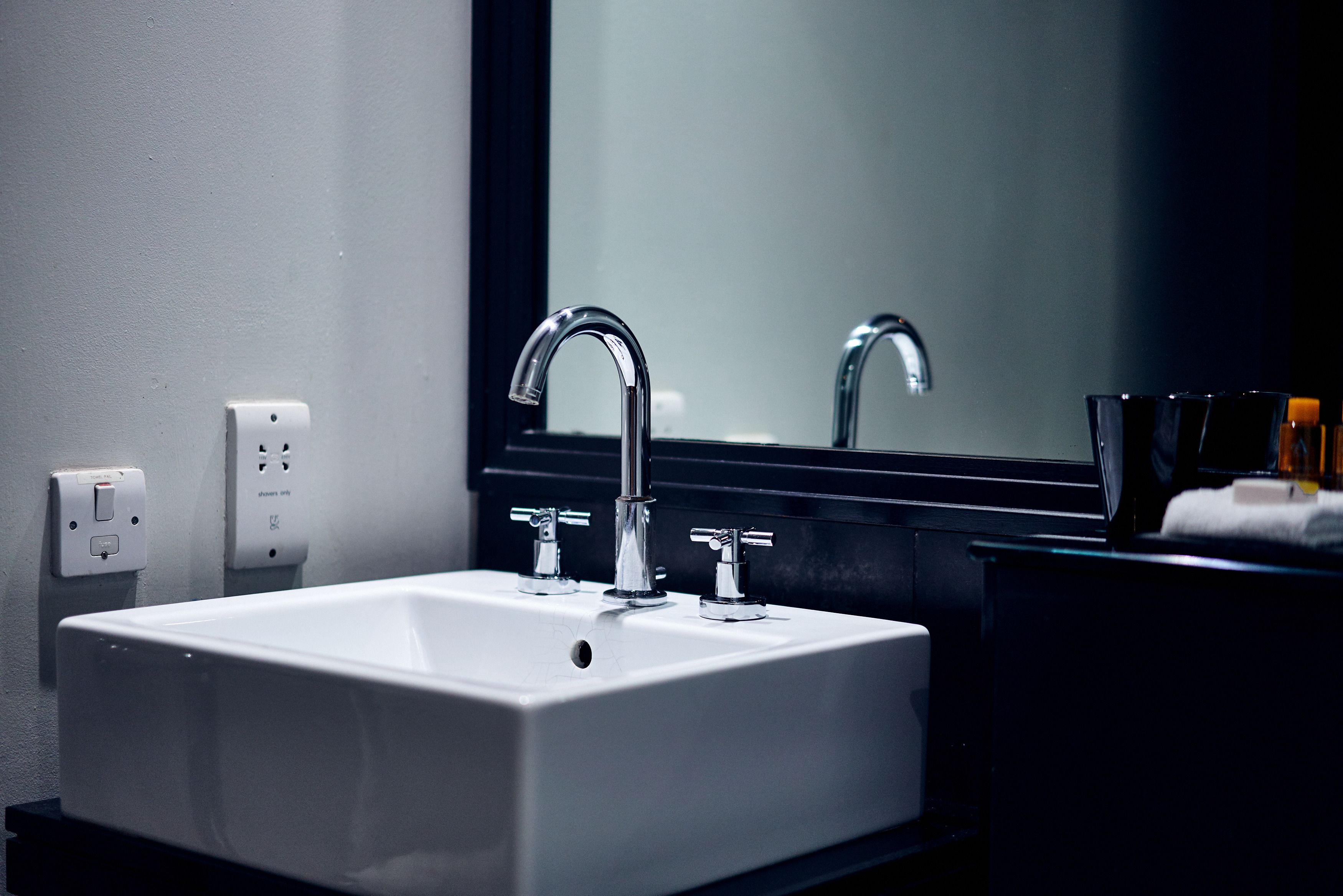 A modern bathroom with a white sink, two chrome faucets, and a mirror above it.