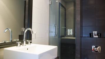 Un baño moderno con un lavamanos blanco, un espejo grande, una ducha con paredes de vidrio y un inodoro.