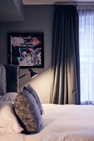 Habitación de hotel con cama, lámpara de escritorio, una obra de arte enmarcada en la pared y ventana con cortinas.