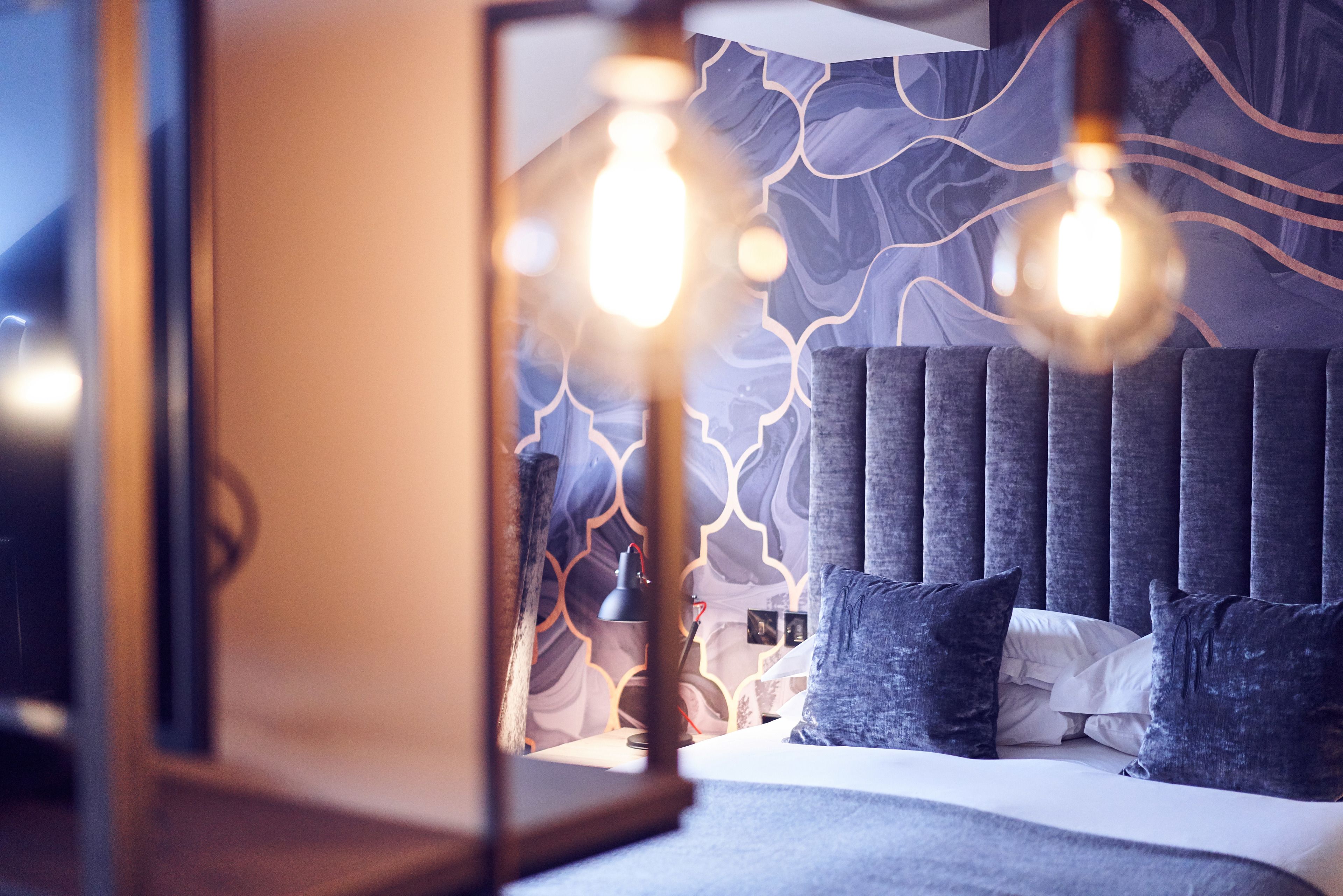 A modern bedroom with a patterned wall, a tufted headboard, and a bedside lamp.