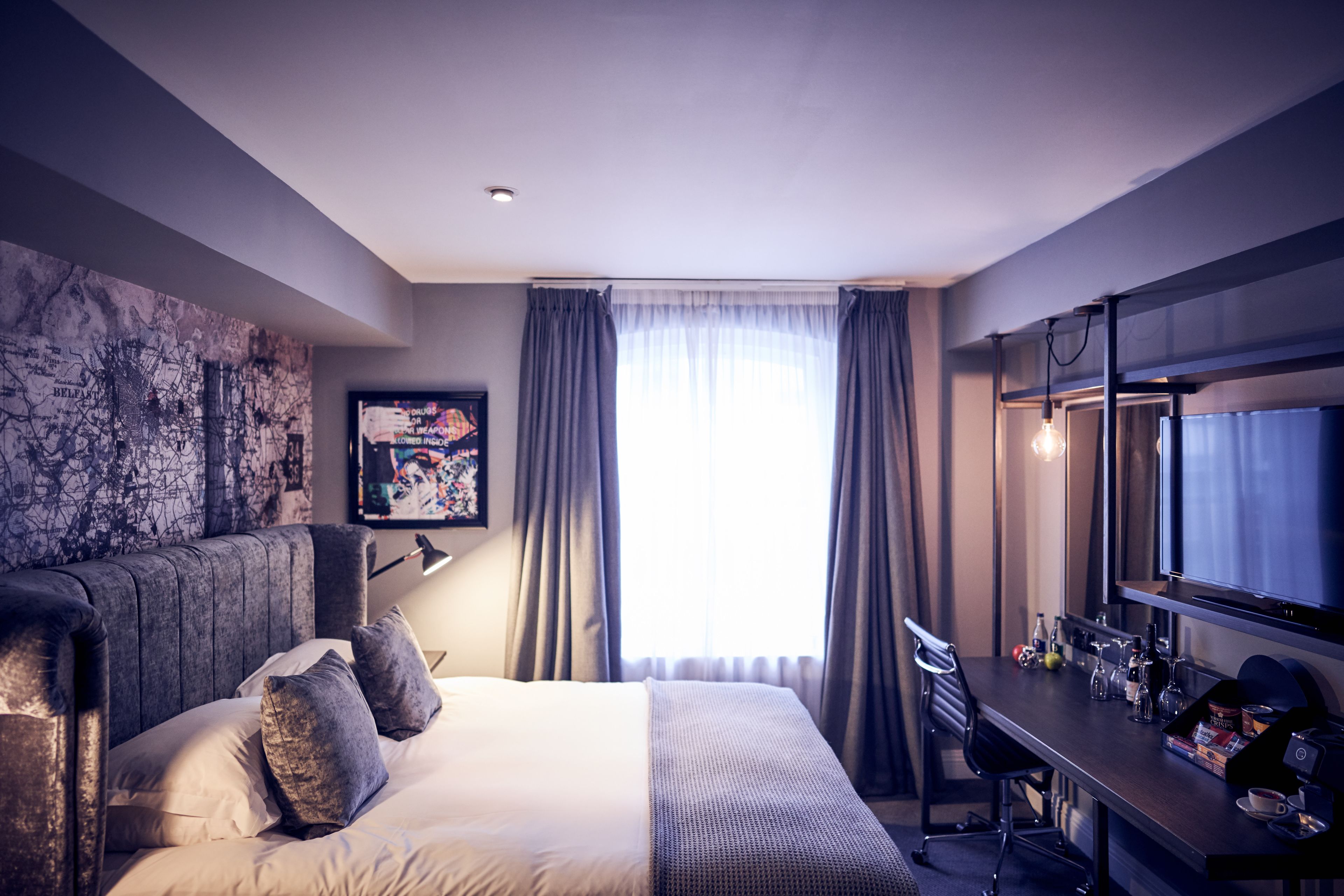 Une chambre d’hôtel moderne dotée d’un grand lit, d’un bureau avec une chaise, d’un téléviseur à écran plat et d’une grande fenêtre avec des rideaux.