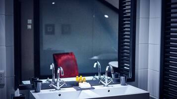 A modern bathroom with a large mirror, two sinks, and a red chair in the background.