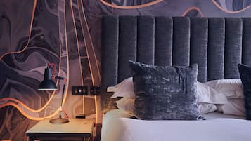 A modern bedroom with a dark headboard, a bedside table with a lamp, and a patterned wall.