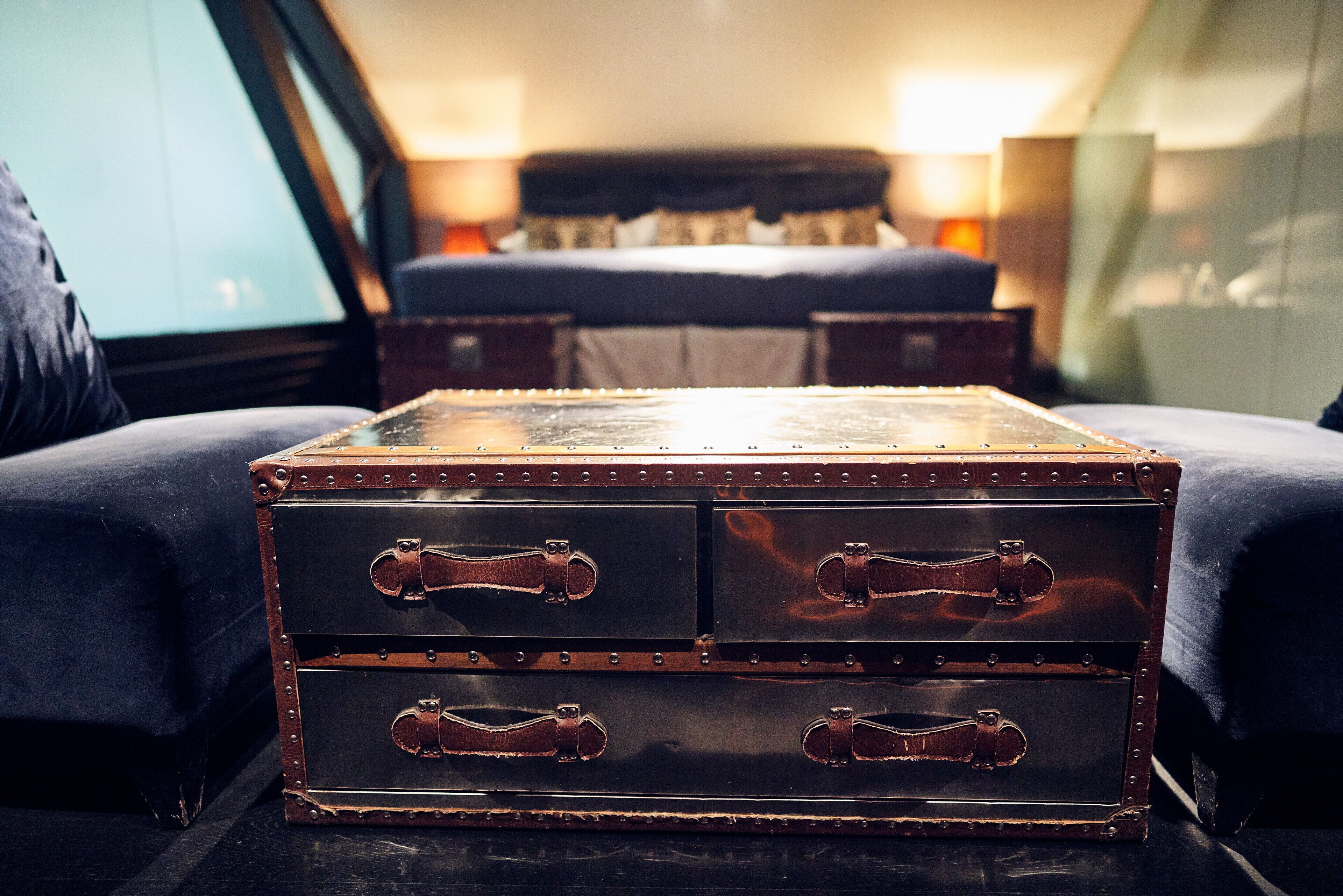 A vintage-style trunk with metal studs and leather handles in a hotel room.