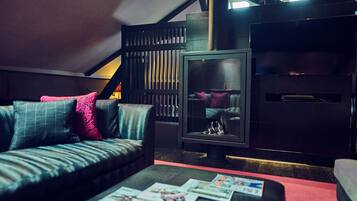 A cozy living room with a sofa, a coffee table with magazines, a fireplace, and a TV.