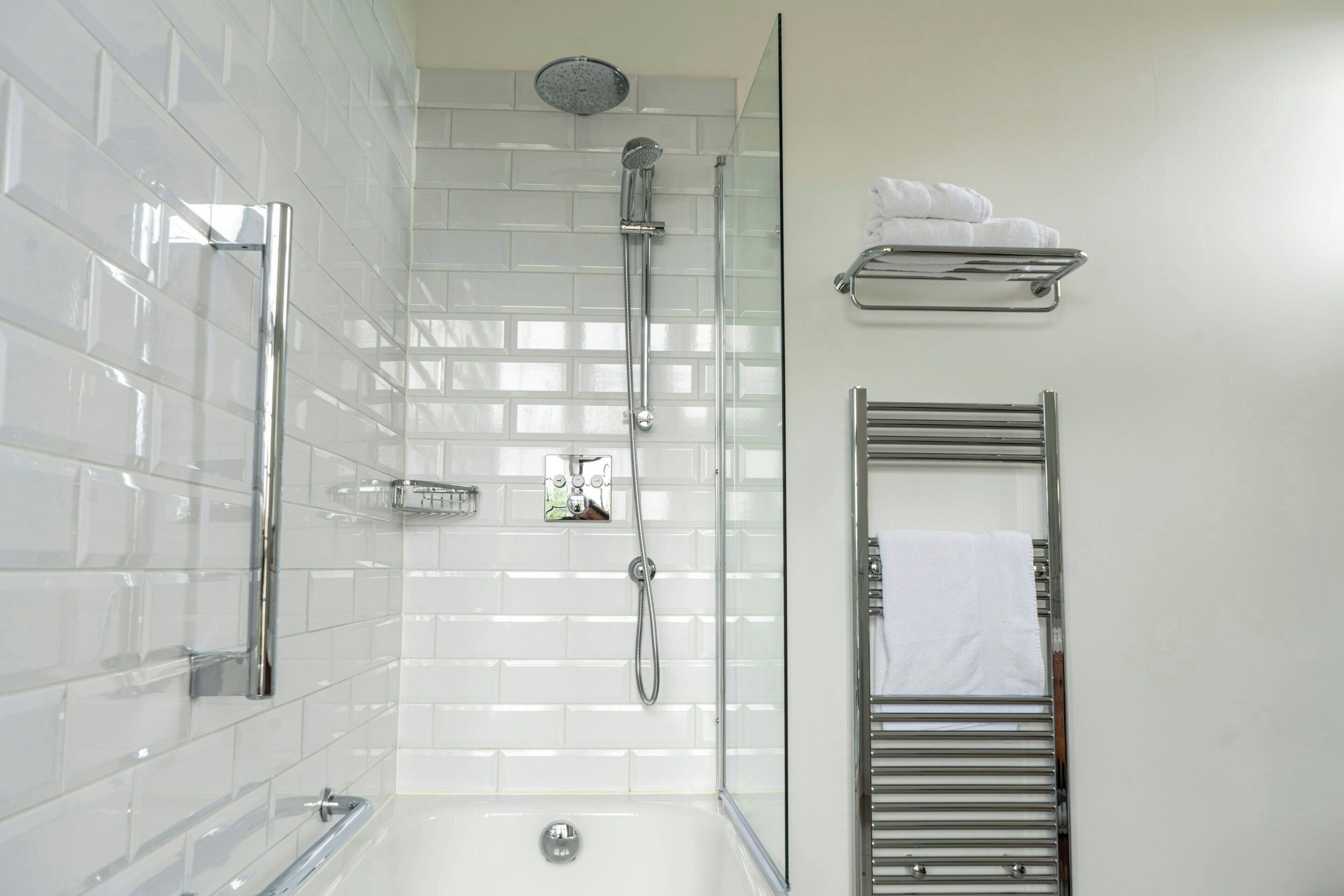 Un baño moderno con ducha acristalada, pared de azulejos blancos, mampara de vidrio y toallero con toallas dobladas.