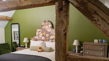Un dormitorio con techo de madera, cama con ropa blanca, pared verde y cabecera con estampado floral.