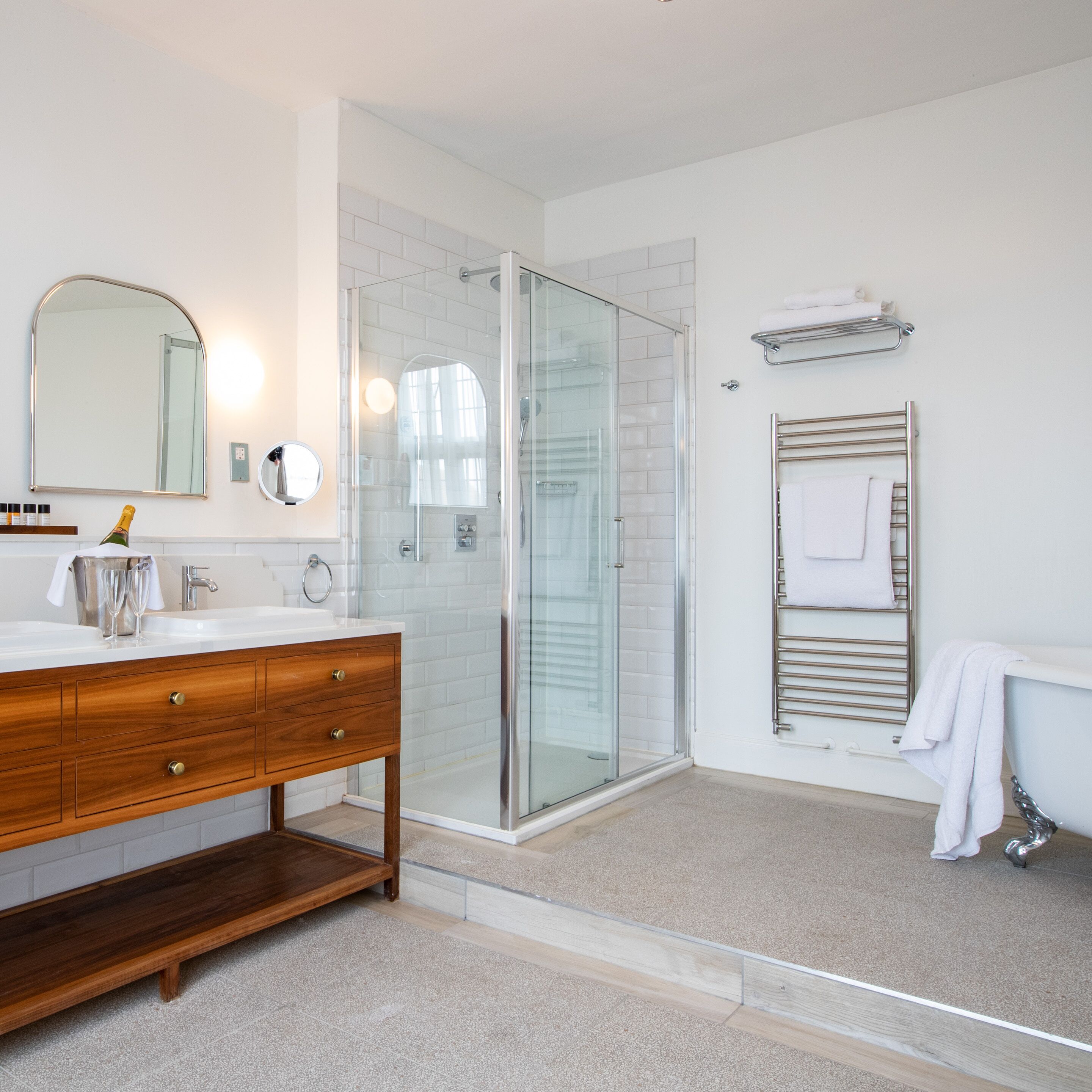 Ein modernes Badezimmer mit Duschkabine aus Glas, einem Holzbadschränkchen mit Waschbecken und einer klassischen Badewanne auf Ziegenfüßen.