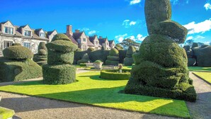 A formal garden with geometrically shaped topiary, a stone pathway, and a historic building with multiple chimneys in the background. - Billesley Manor Hotel & Spa, a Tribute Portfolio Hotel (Alcester)
