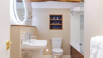 A bathroom with a white sink, a toilet, a wooden shelf with toiletries, and a glass shower enclosure.