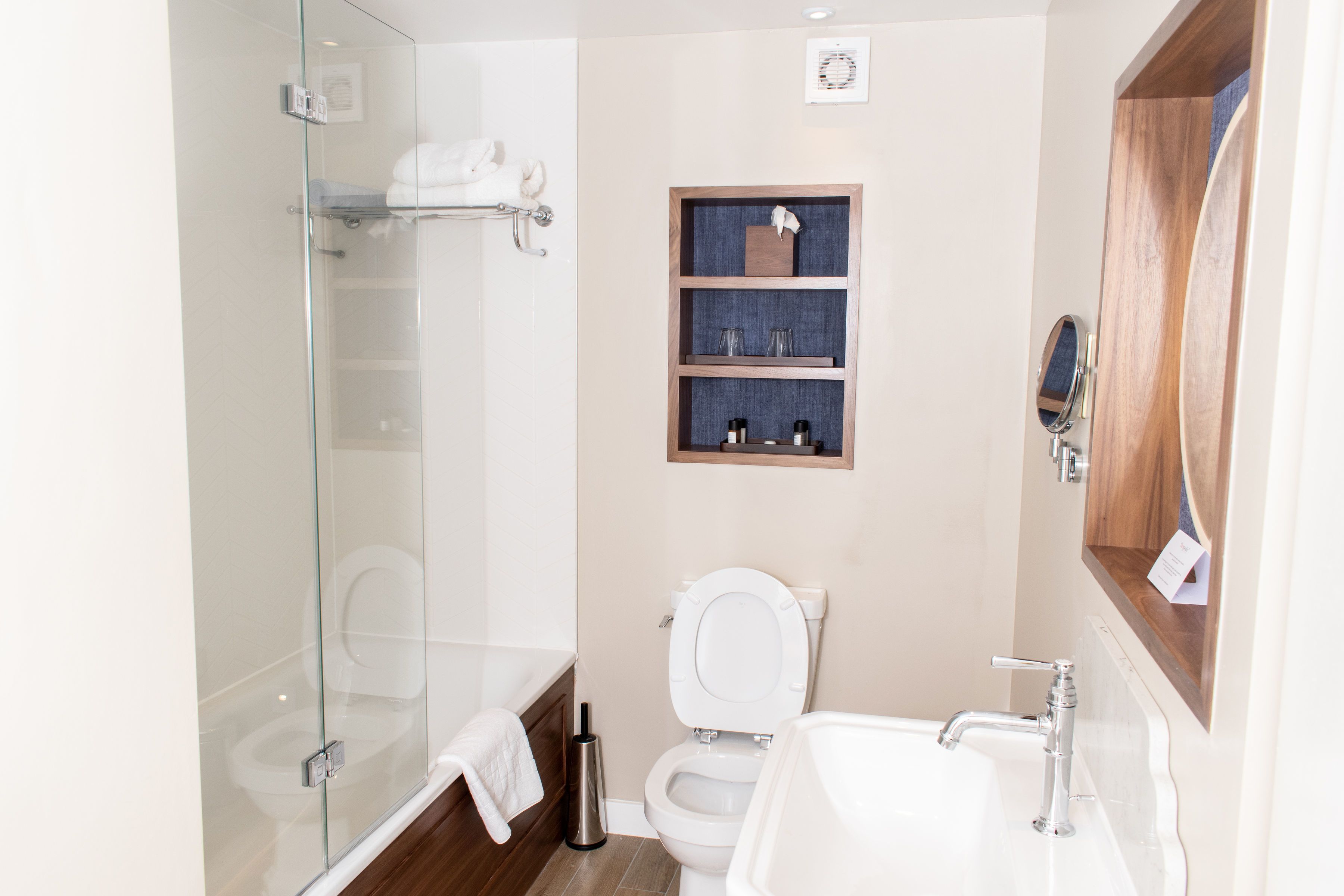 A modern bathroom with a glass shower enclosure, a white toilet, and a wooden vanity with a mirror.