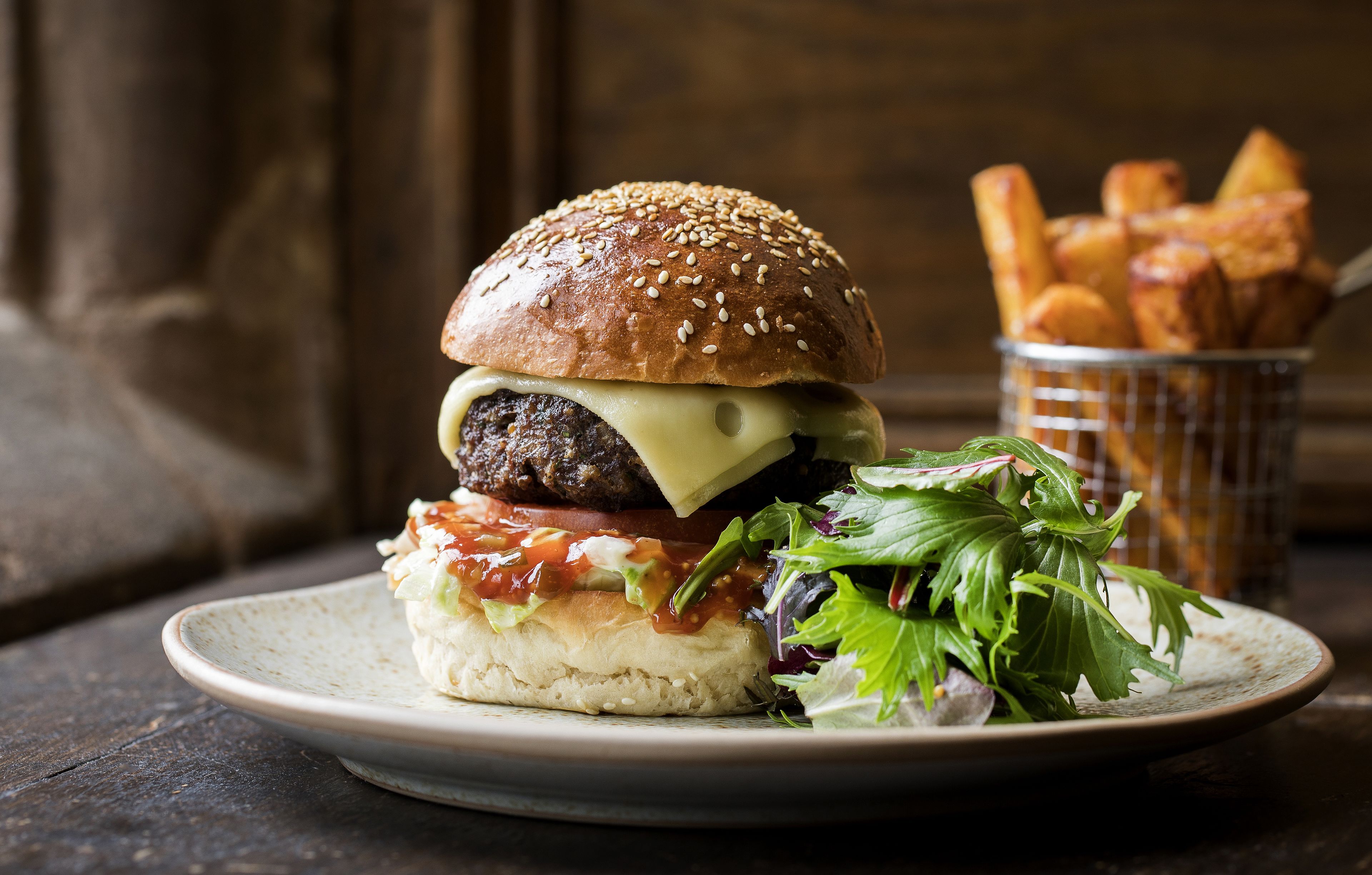 Een hamburger met sla, tomaat en kaas in een broodje, vergezeld van friet en een salade op een bord.