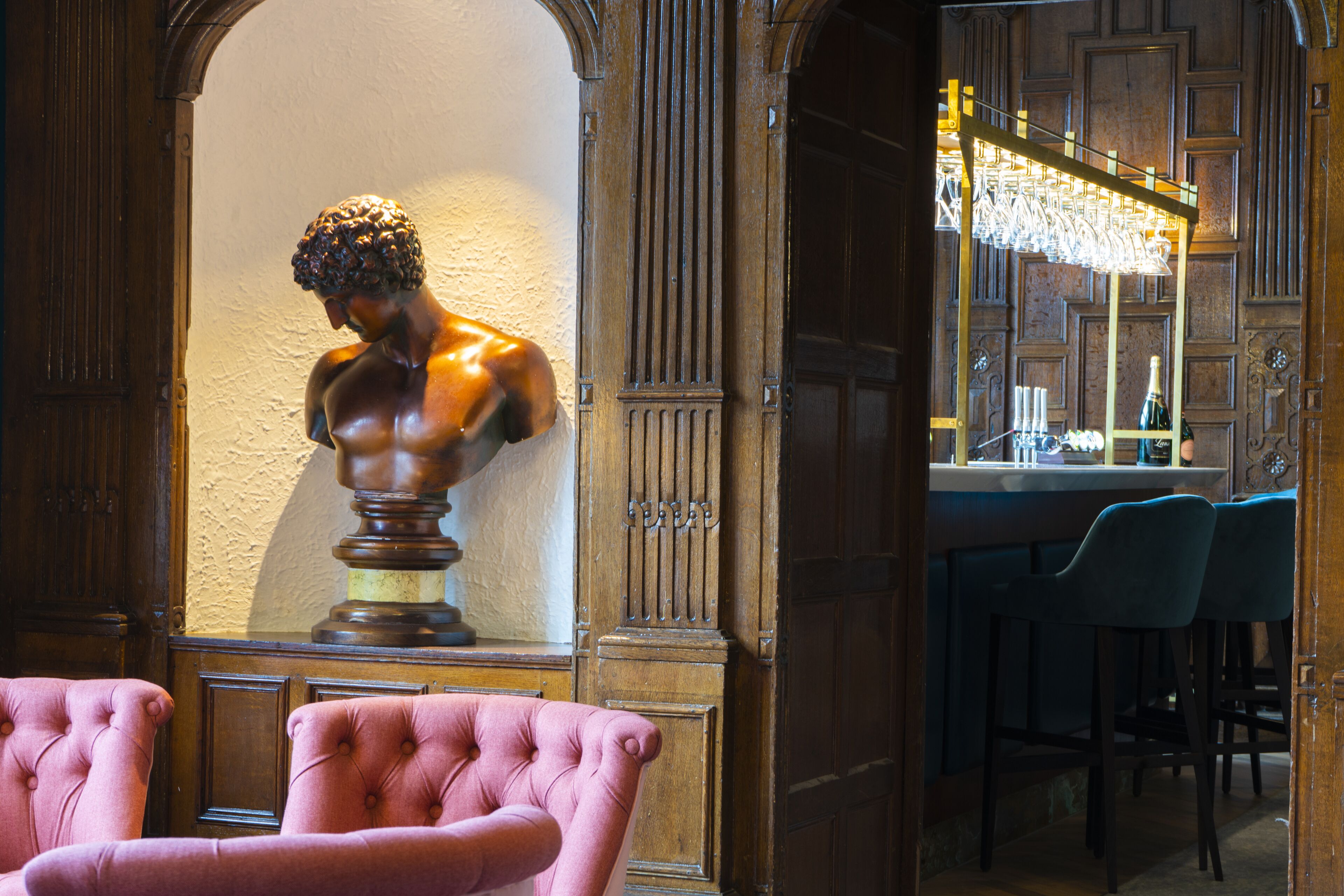 A bar area with a bust sculpture, bar stools, and a chandelier.