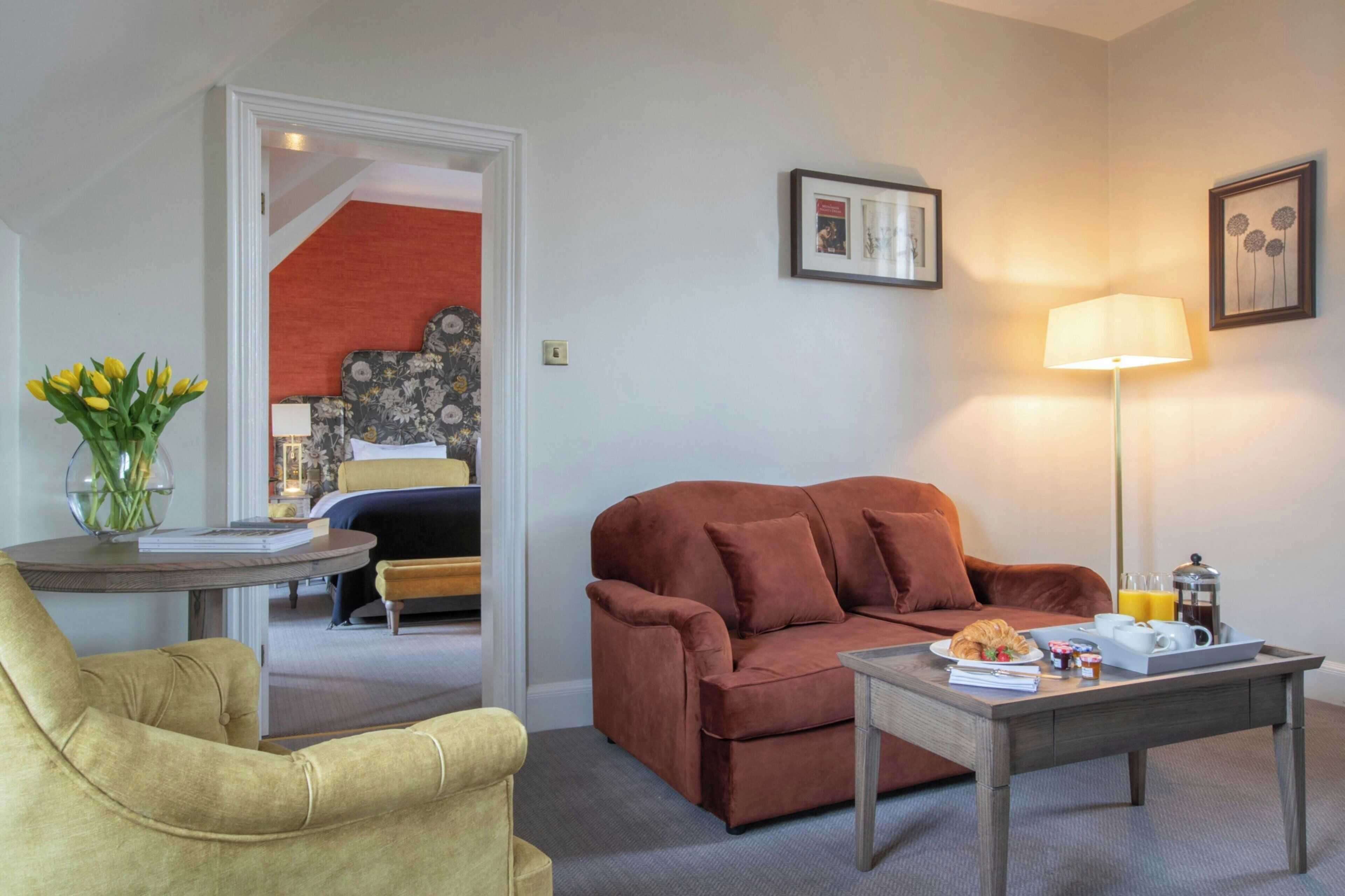 Ein Wohnzimmer mit einem braunen Sofa, einem gelben Sessel, einem Couchtisch mit Frühstücksangeboten und einer Lampe.